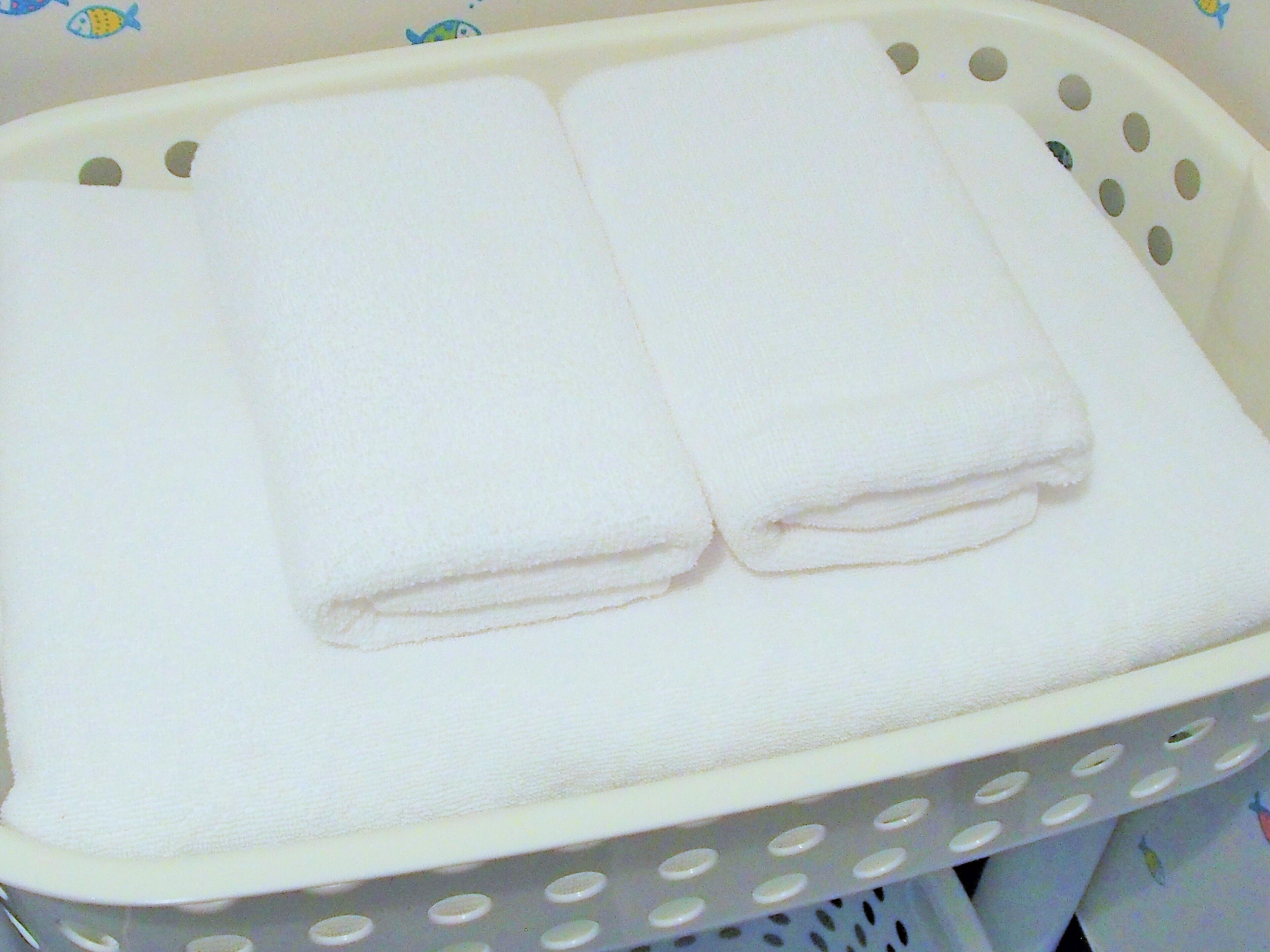 A white laundry basket with a perforated edge, containing folded white towels.