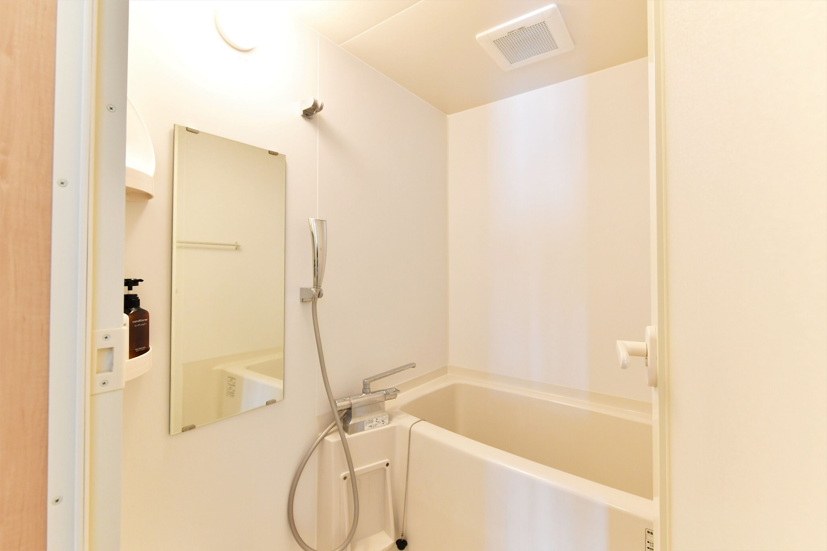 A bathroom with a bathtub, a shower, a mirror, and a hand sanitizer dispenser.