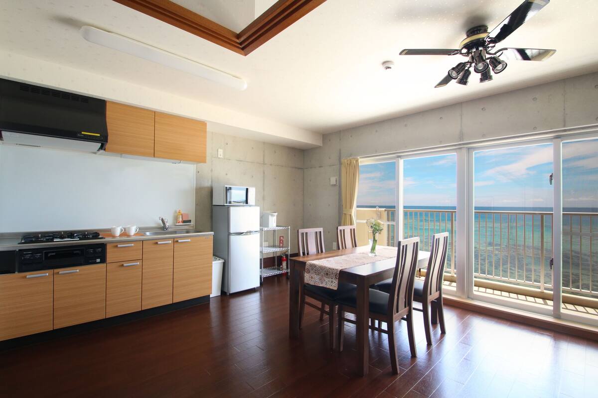 Una cocina moderna con armarios de madera, un comedor con mesa y sillas, y un ventanal con vista al océano.