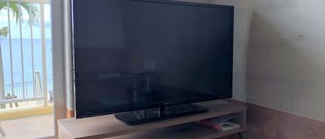 A flat-screen TV on a wooden stand in a room with a balcony.