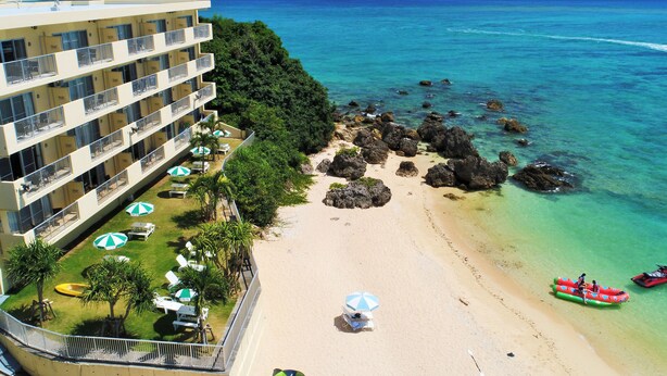 Un hotel con varios balcones con vistas a una playa de aguas cristalinas y rocas.