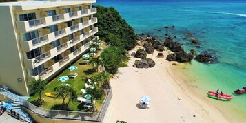 Un hotel con varios balcones con vistas a una playa de aguas cristalinas y rocas.