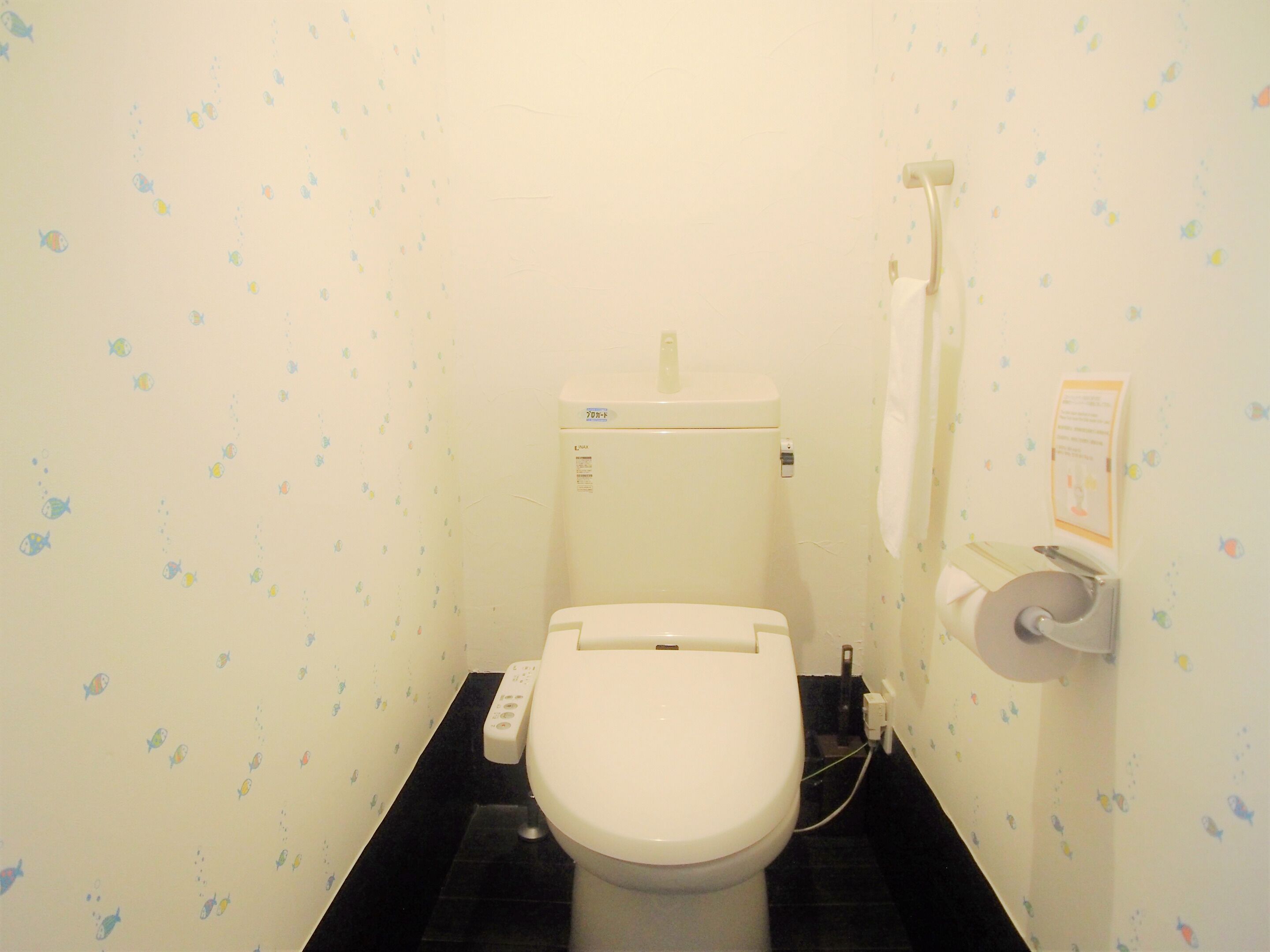 A small, compact bathroom with a toilet, a paper towel dispenser, and a wall-mounted towel rack.