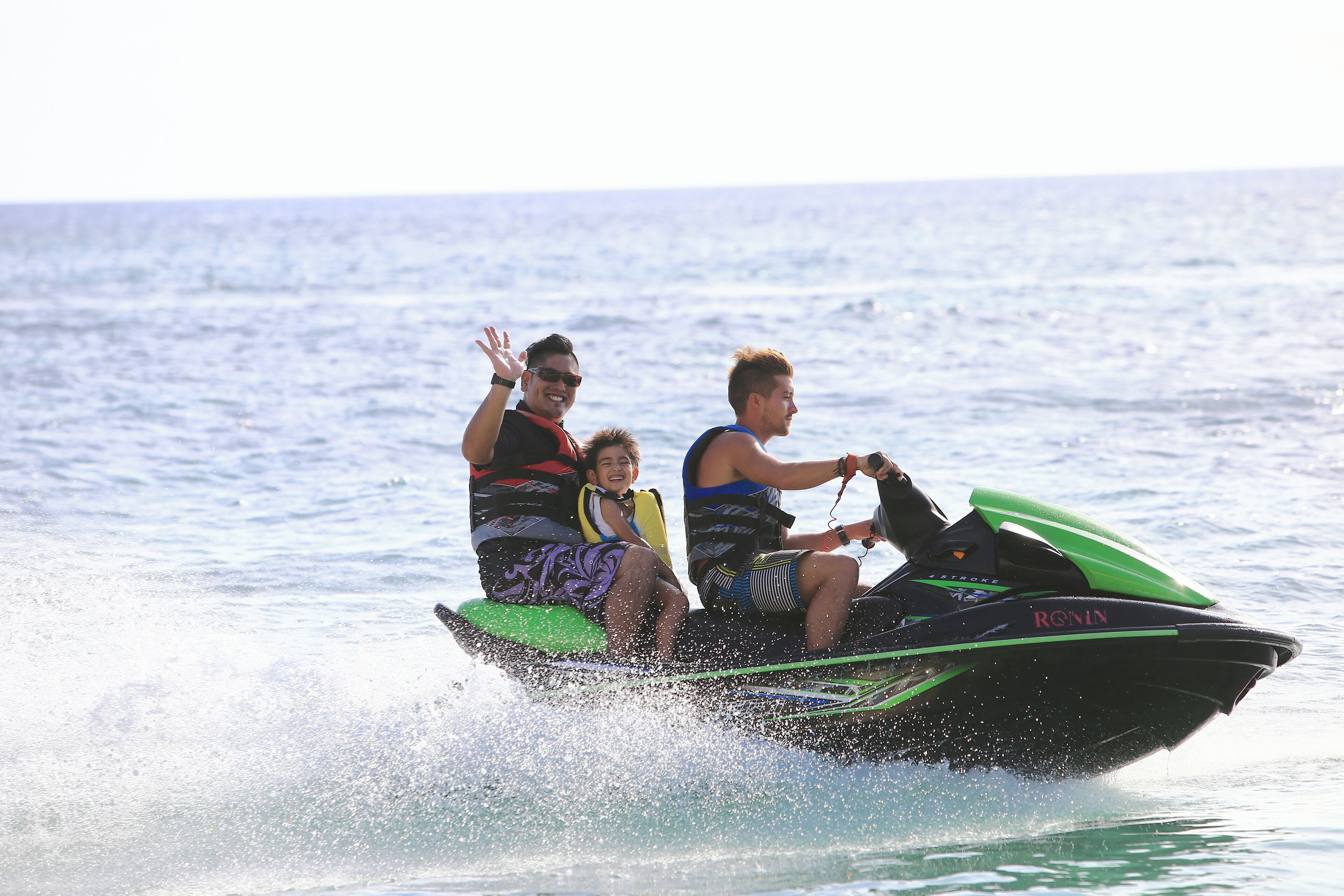 Two people on a jet ski with a child, water splashing around.