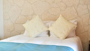 Ein Bett mit weißblauer Bettdecke, zwei Kissen und einer Steinwand im Hintergrund.