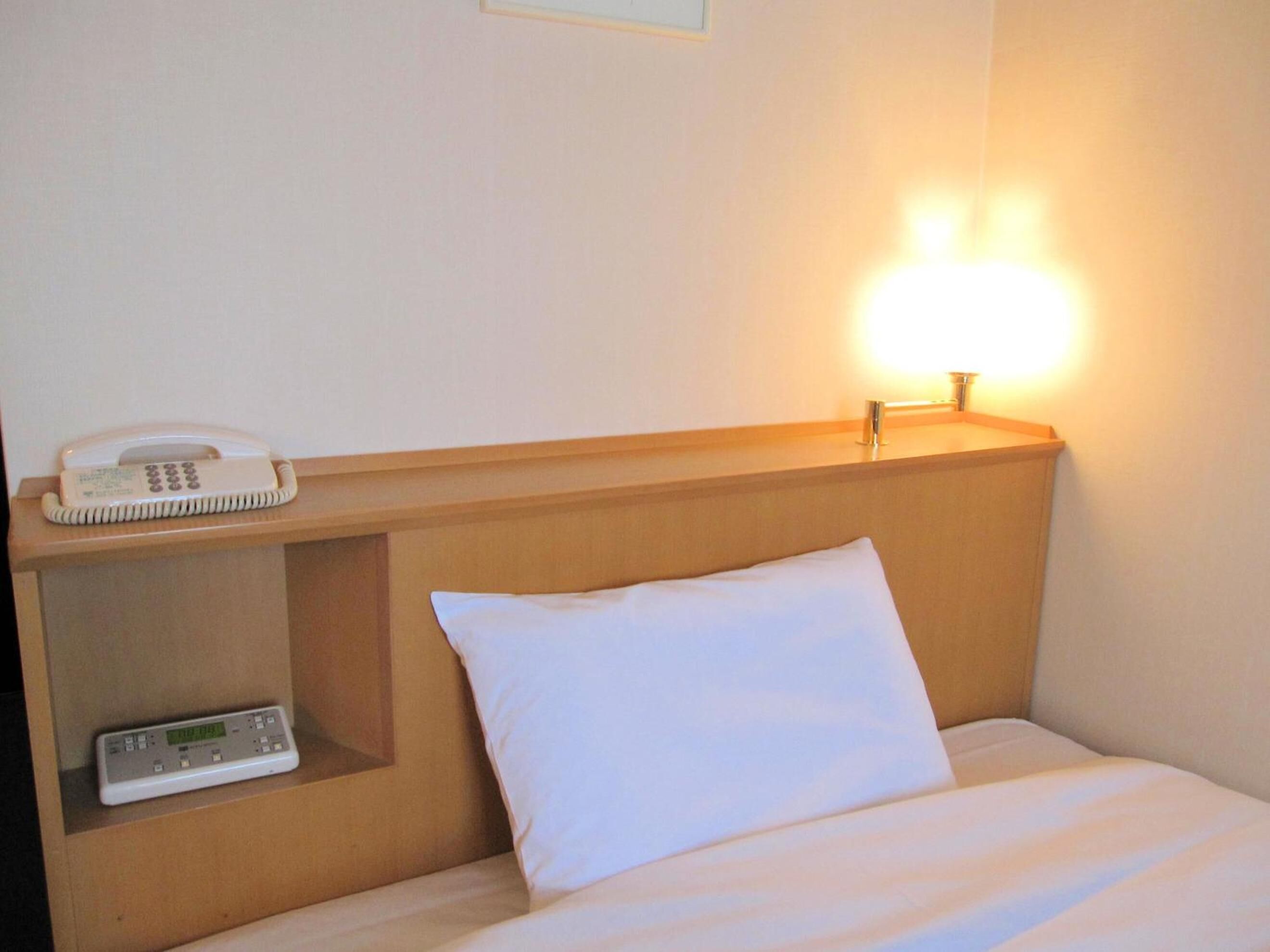 Une chambre d’hôtel avec un lit, un téléphone sur la table de chevet et une horloge numérique posée sur une étagère.