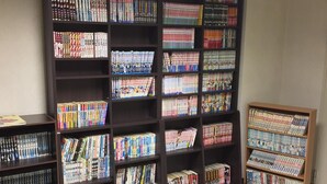 A bookcase filled with various books, a sign above it, and a small table with books on it. - Hotel Crown Hills Kofu (Kofu)