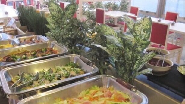 A buffet area with various food options in metal trays, surrounded by red cushioned chairs and tables. - Hotel Crown Hills Kofu (Kofu)