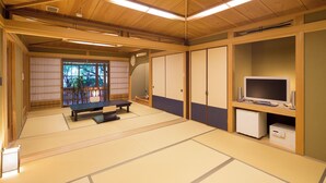 Una habitación japonesa tradicional con suelo de tatami, una mesa baja de tatami, puertas correderas y un televisor.