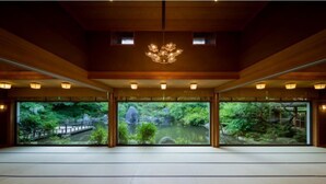Una habitación amplia con ventanas grandes, vigas de madera y una lámpara decorativa en el techo.