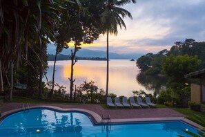A swimming pool with lounge chairs and a view of a calm lake at sunset. - Oruthota Chalets (Maberiyatenna)