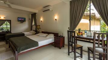 A hotel room with two beds, a TV, a desk with a chair, a balcony with a table and chairs, and a view of greenery.