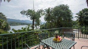 A balcony with a table and chairs, overlooking a lake and mountains. - Oruthota Chalets (Maberiyatenna)