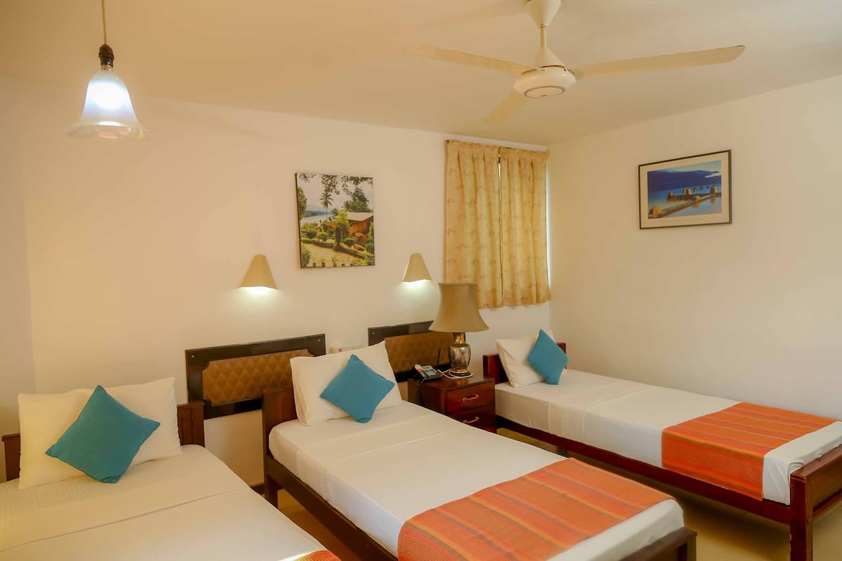 A hotel room with two single beds, a ceiling fan, a nightstand with a lamp, and two wall-mounted lamps.
