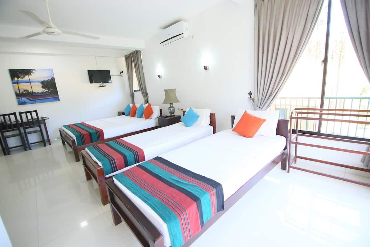 A hotel room with two beds, a TV, an air conditioner, and a balcony with a railing.