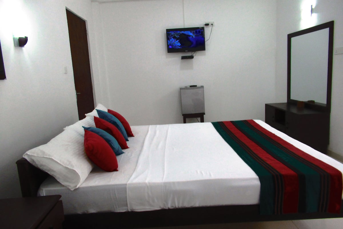 A hotel room with a bed, pillows, a television, a mirror, and a small cabinet.