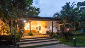 A hotel entrance with a covered porch, steps leading up to the entrance, and a well-maintained garden with palm trees and other greenery. - Oruthota Chalets (Maberiyatenna)