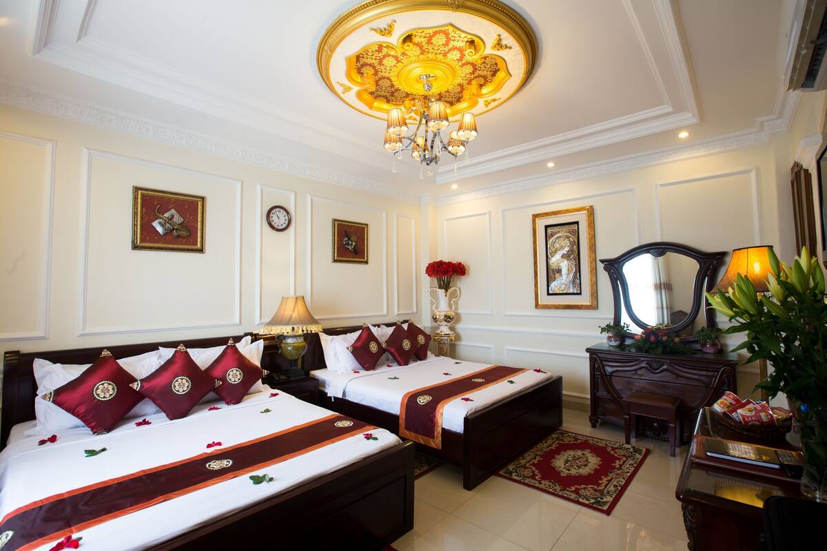 A hotel room with two beds, a chandelier, a desk, and a mirror.