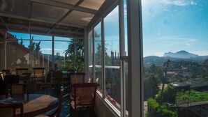 Una habitación con ventanas amplias, muebles de mimbre y vista a un paisaje montañoso.