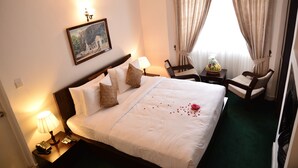 Habitación de hotel con una cama grande, dos mesitas de noche, una silla, un escritorio, una lámpara, un cuadro en la pared y una ventana con cortinas.
