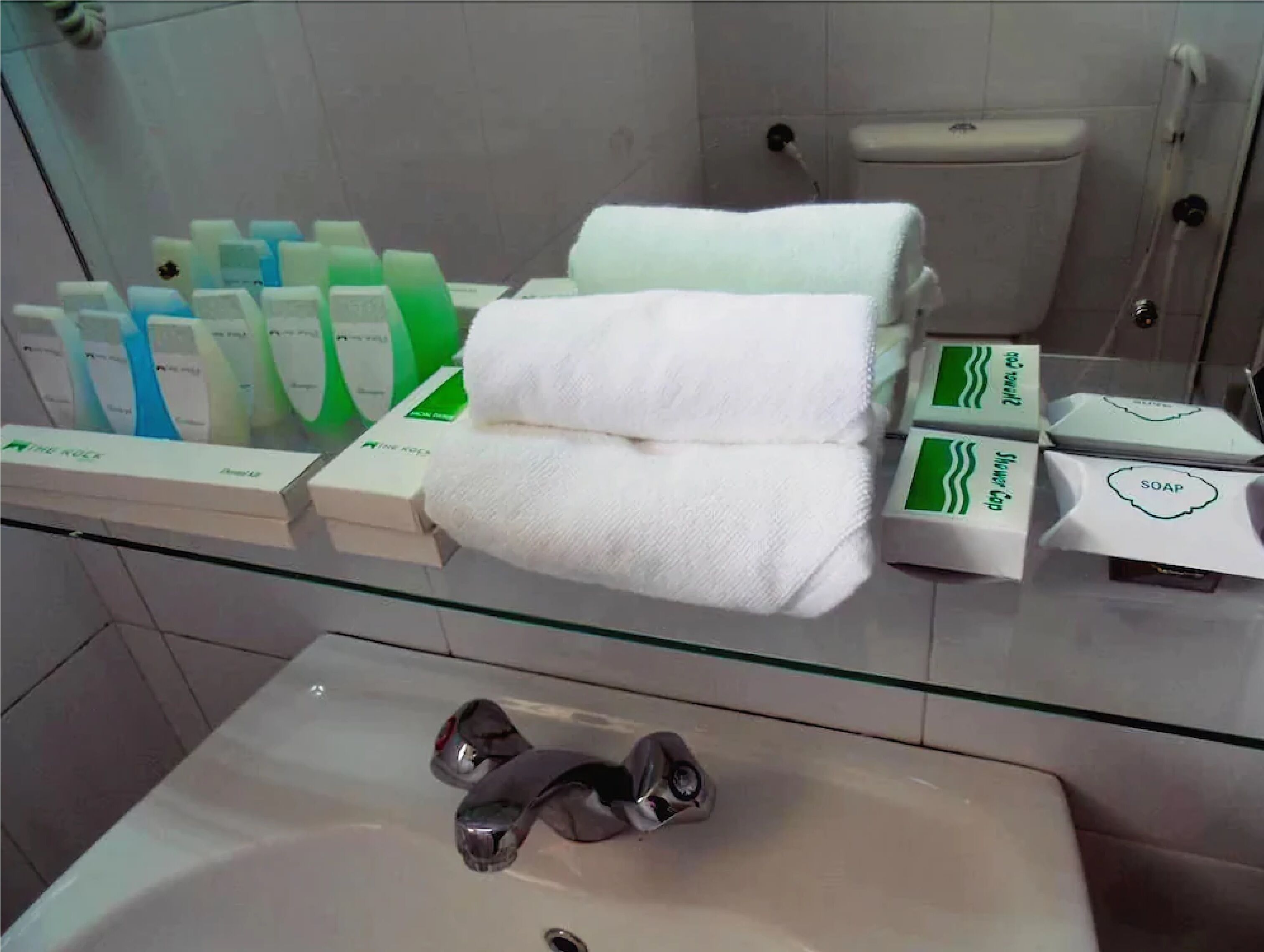 Une salle de bain avec une étagère en verre où sont exposés les articles de toilette, un lavabo blanc et des toilettes.