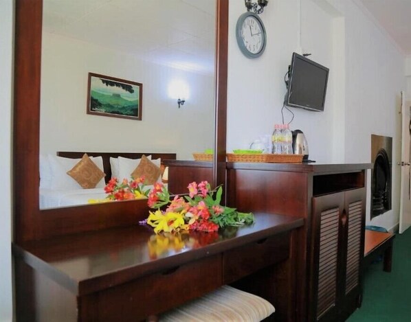 Habitación de hotel con un escritorio de madera, un espejo, un reloj, un televisor y una cama con almohadas.