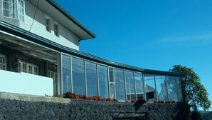 Una casa moderna con una amplia estructura de vidrio, cimientos de piedra y un cielo azul despejado.