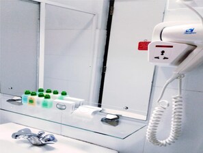 Et badeværelse med en glashylde til toiletartikler, et spejl og en hårtørrer på en vægmonteret opladningsstation.