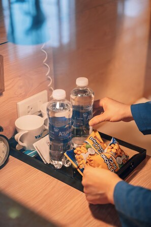 A tray with water bottles, a mug, and snack packets on a wooden surface. - VATC SleepPod Terminal 1 (Hanoi)