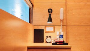 Une table de chevet en bois avec une lampe, un téléphone, une horloge et un flacon de gel hydroalcoolique.