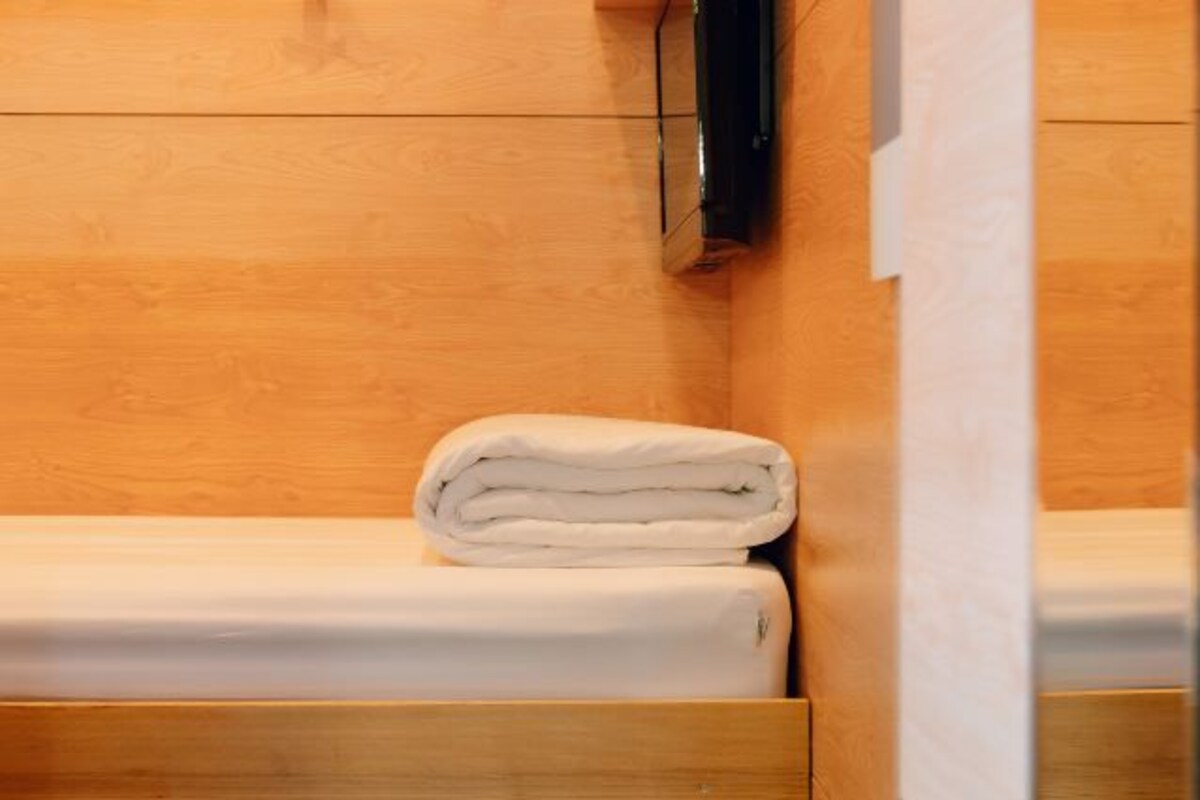 Ein Zimmer mit Holzboden, einem Bett, einem an der Wand befestigten Flachbildfernseher und einem gefalteten weißen Handtuch auf dem Bett.