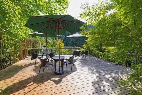 Une terrasse extérieure avec un plancher en bois, des chaises en métal et une table placée sous un parasol vert.