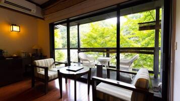 A room with a large window, wooden flooring, and furniture including a sofa and chairs.