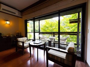 Ein Zimmer mit großem Fenster, Holzboden und Möbeln, darunter ein Sofa und Sessel.