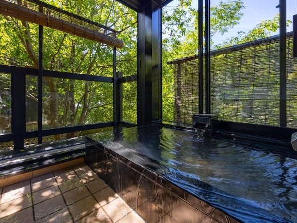A hot tub area with a view of trees through large windows. - Takedao Onsen Koyokan Bettei Azale (Takarazuka)