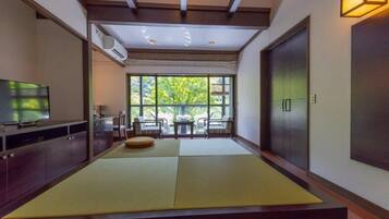 A room with tatami mats, a television, a dining area with chairs, and a view through large windows.