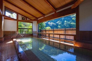 Un onsen japonais traditionnel, avec des poutres en bois, une grande fenêtre et une clôture en bambou.