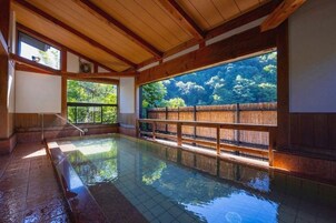 Un onsen japonés tradicional con vigas de madera, un ventanal grande y una cerca de bambú.