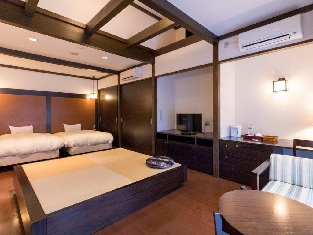 A hotel room with a bed, a desk, a chair, a television, and an air conditioning unit.