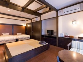 Una habitación de hotel con cama, escritorio, silla, televisor y aire acondicionado.