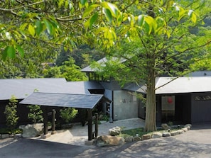 A modern building with a covered entrance and a tree in front. - Takedao Onsen Koyokan Bettei Azale (Takarazuka)