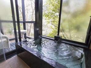 Un bain à remous doté d’une paroi en verre, entouré de fauteuils en osier, et offrant une vue sur les arbres à l’extérieur.