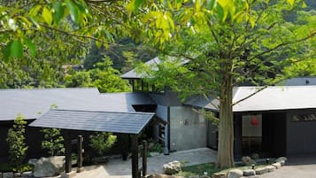 A modern building with a sloped roof, surrounded by greenery and trees.