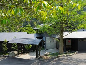 A modern building with a sloped roof, surrounded by greenery and trees. - Takedao Onsen Koyokan Bettei Azale (Takarazuka)