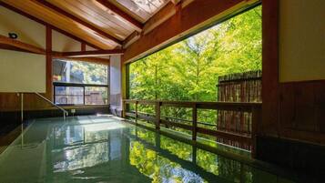 An indoor swimming pool with a wooden ceiling and a large window offering a view of trees.