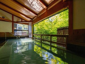 An indoor swimming pool with a wooden ceiling and a large window offering a view of trees. - Takedao Onsen Koyokan Bettei Azale (Takarazuka)