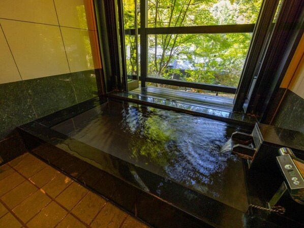 Una habitación con un ventanal grande, una bañera negra y suelo de baldosas.