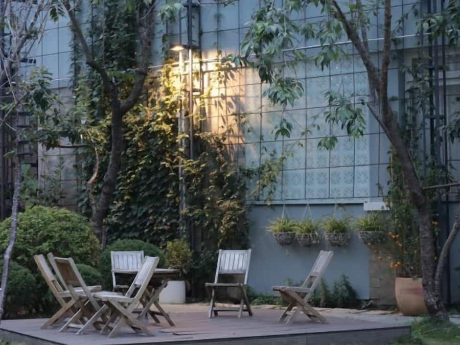An outdoor seating area with chairs and tables, surrounded by greenery and a building with a grid-like facade.