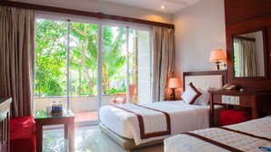 A hotel room with a large bed, a desk, a chair, and a view of lush greenery through the window. - Hoa Binh Phu Quoc Hotel (Phu Quoc)