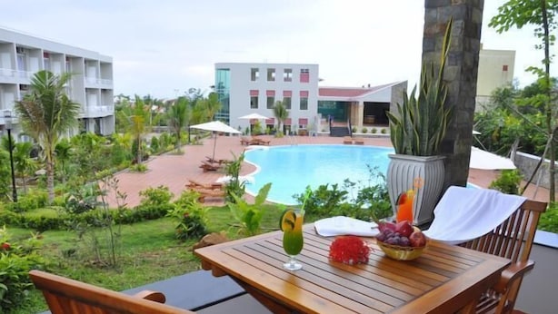 A wooden table with a drink and fruit bowl, overlooking a swimming pool with a building in the background. - Hoa Binh Phu Quoc Hotel (Phu Quoc)